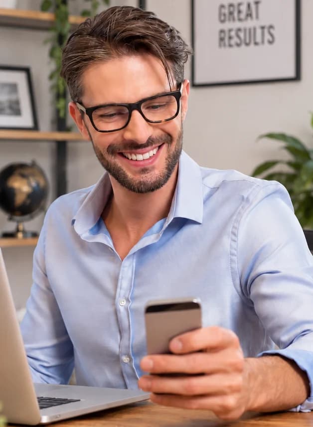 A smiling man checking his phone at his desk